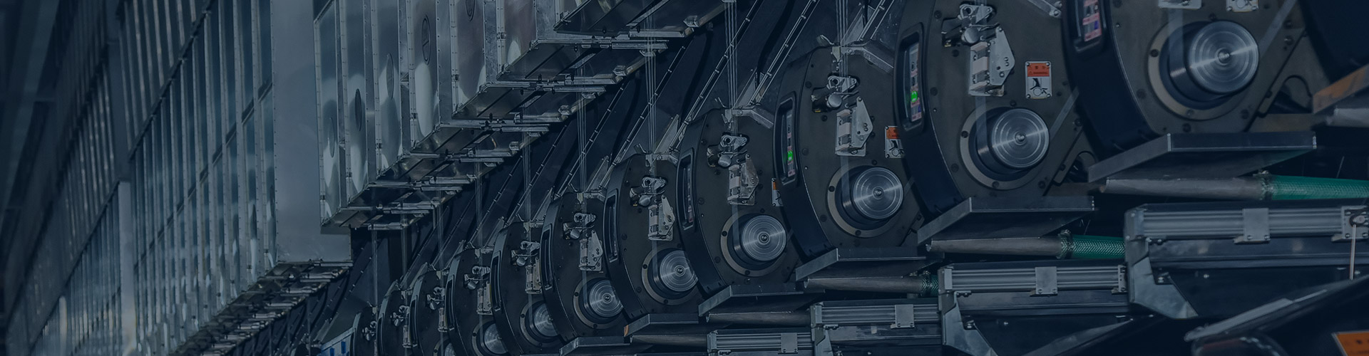 Close-up view of industrial machinery with rows of metal wheels and mechanical gears, lit in deep navy-blue tones with a focused, technical mood