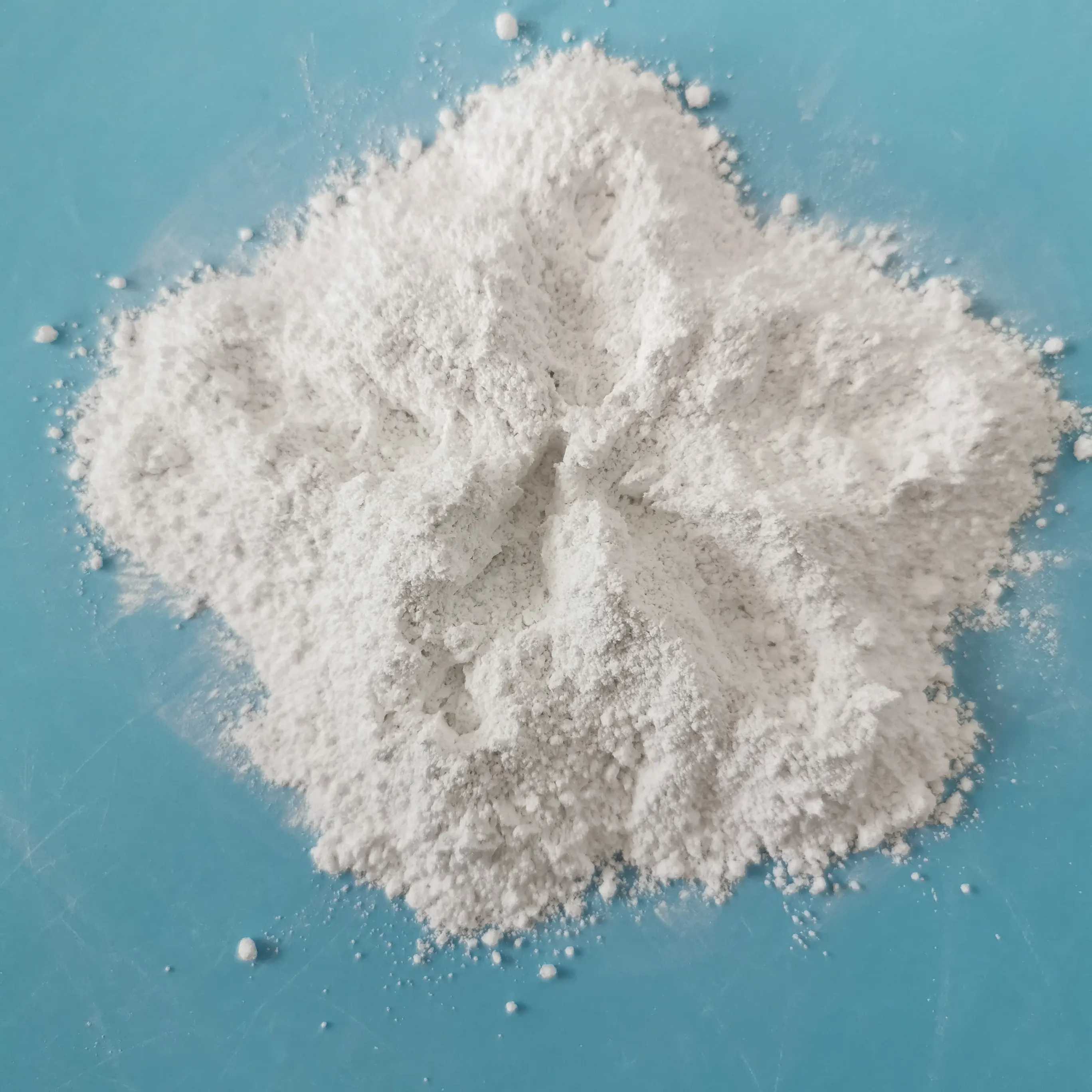 Close-up of a pile of fine white powder on a teal surface, minimalist product shot